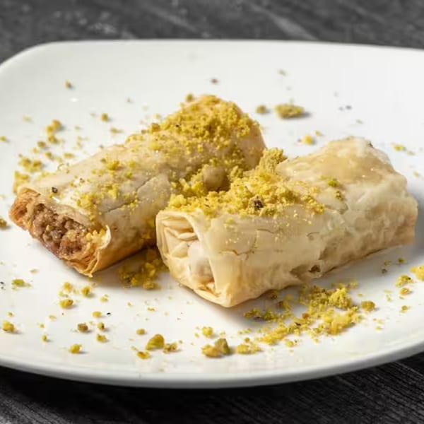 Two pieces of Lebanese baklava, sprinkled with green pistachios, on a white plate.