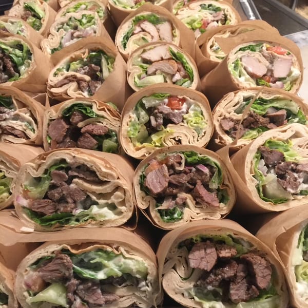 Close-up of numerous Lebanese wraps, some with chicken and others with beef, lettuce, and sauce.