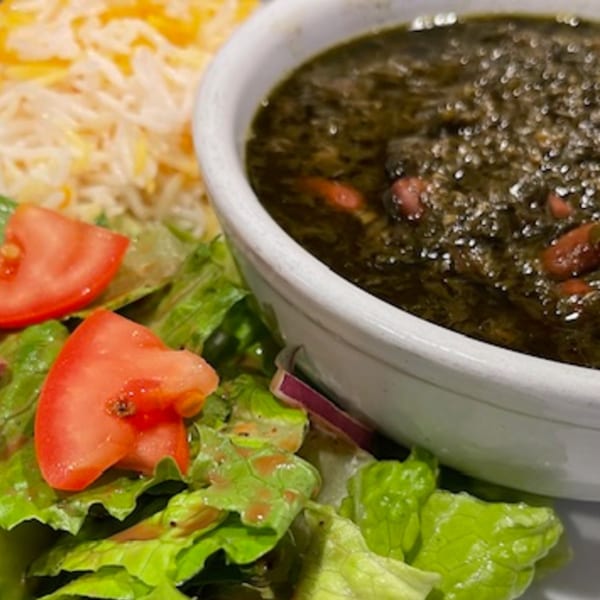 Lebanese dish with a bowl of dark green stew, rice, and a fresh green salad with tomatoes.