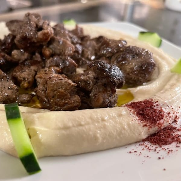 Lebanese hummus topped with seasoned meat, olive oil, sumac, and cucumber slices.