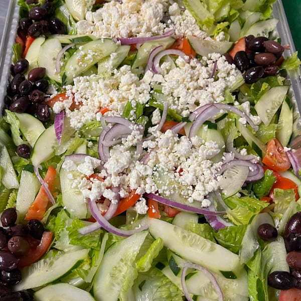 A vibrant Lebanese salad with lettuce, cucumbers, tomatoes, red onions, black olives, and crumbled feta cheese.