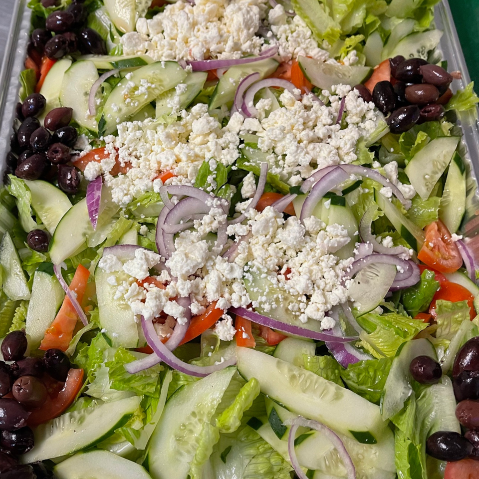 A vibrant Lebanese salad with lettuce, cucumbers, tomatoes, red onions, black olives, and crumbled feta cheese.