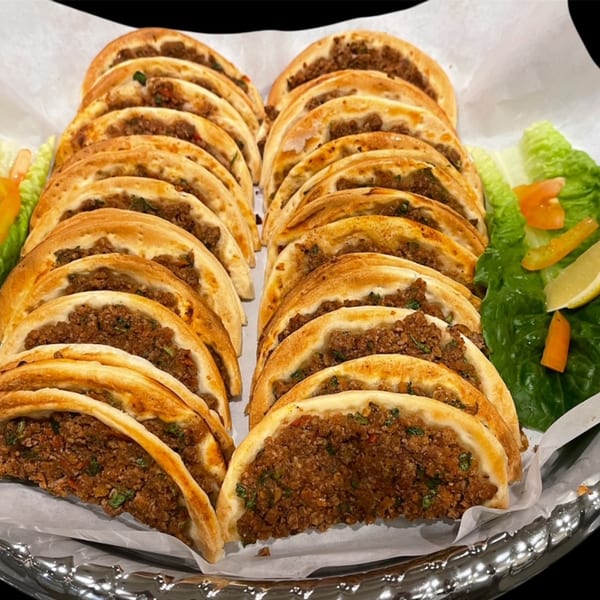 A tray of Lebanese meat pies (fatayer) with lettuce, tomato, and lemon garnish.