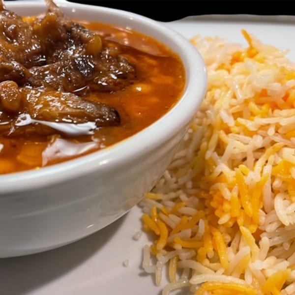 Lebanese stew with meat and vegetables in a white bowl, served with yellow and white rice.