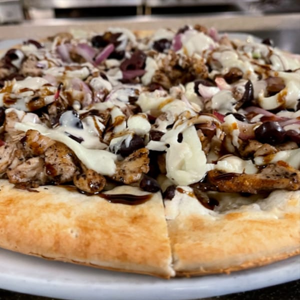 A close-up of a Lebanese pizza topped with chicken, red onions, olives, and white and dark sauces.