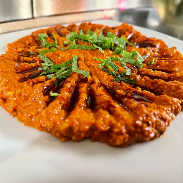 A vibrant orange Lebanese muhammara dip, garnished with fresh mint and a drizzle of olive oil.